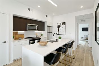 A modern kitchen with white countertops and black chairs.